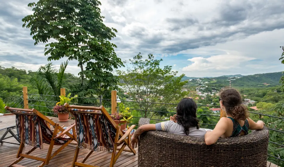 Two people seen from behind on a deck, looking out over the town and green hills