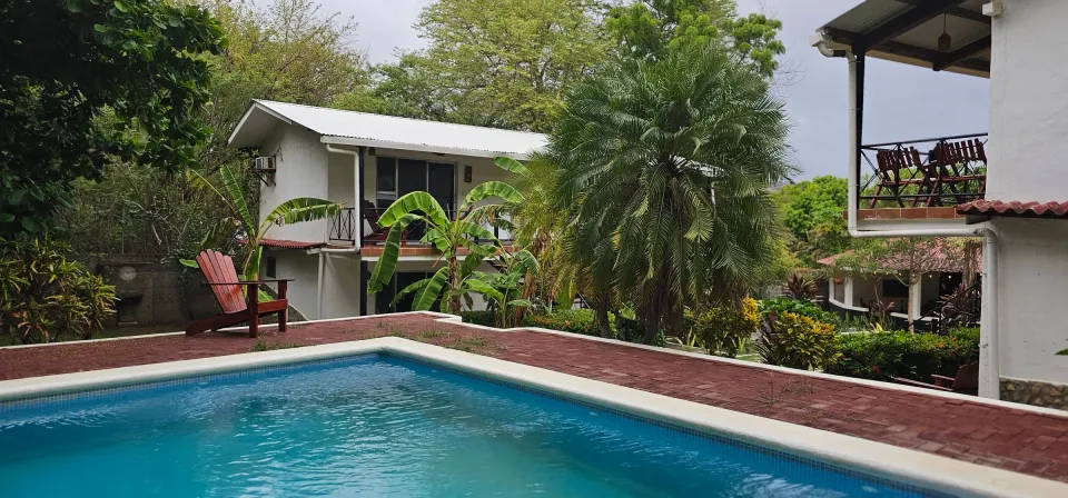 A small pool edged in red tile, palms and a white building with balconies behind